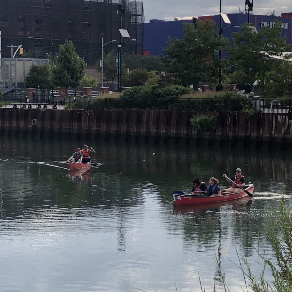 students and guides in red canoes paddle in the Gowanus Canal