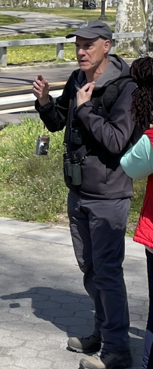 Ken Chaya standing next to a tree wearing binoculars.