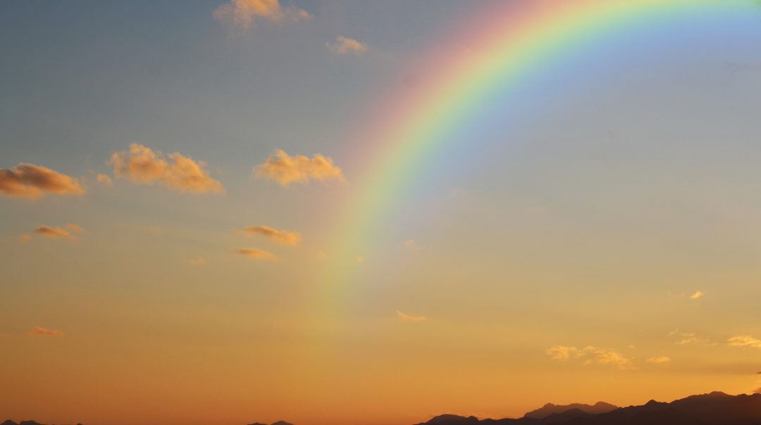 A rainbow over a sky fading from blue to golden