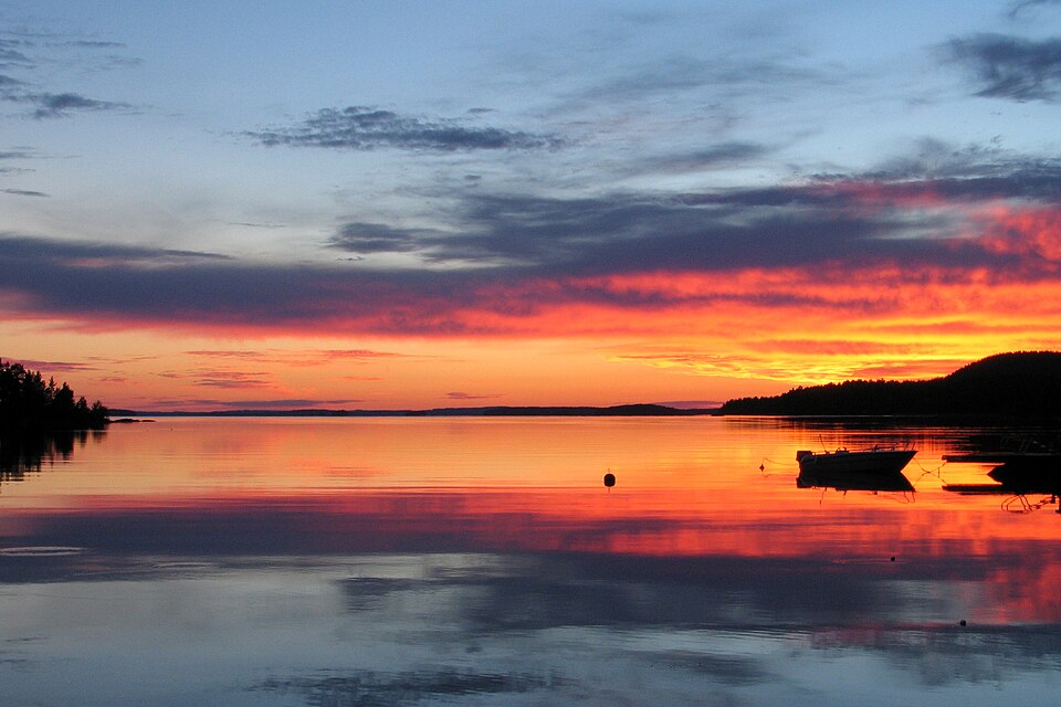 A beautiful orange sunset over a lake with land and trees on both sides