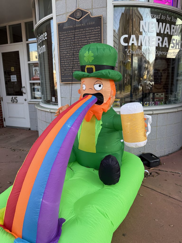 A blow-up leprechaun with a beer in his hand, actively throwing up a rainbow.