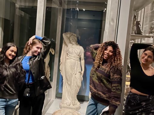 Four students stand with a white marble statue mimicking the statue's pose