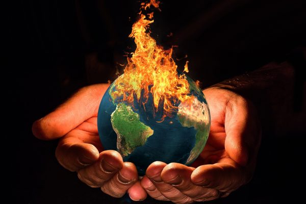two hands holding out an earth ablaze against dark background