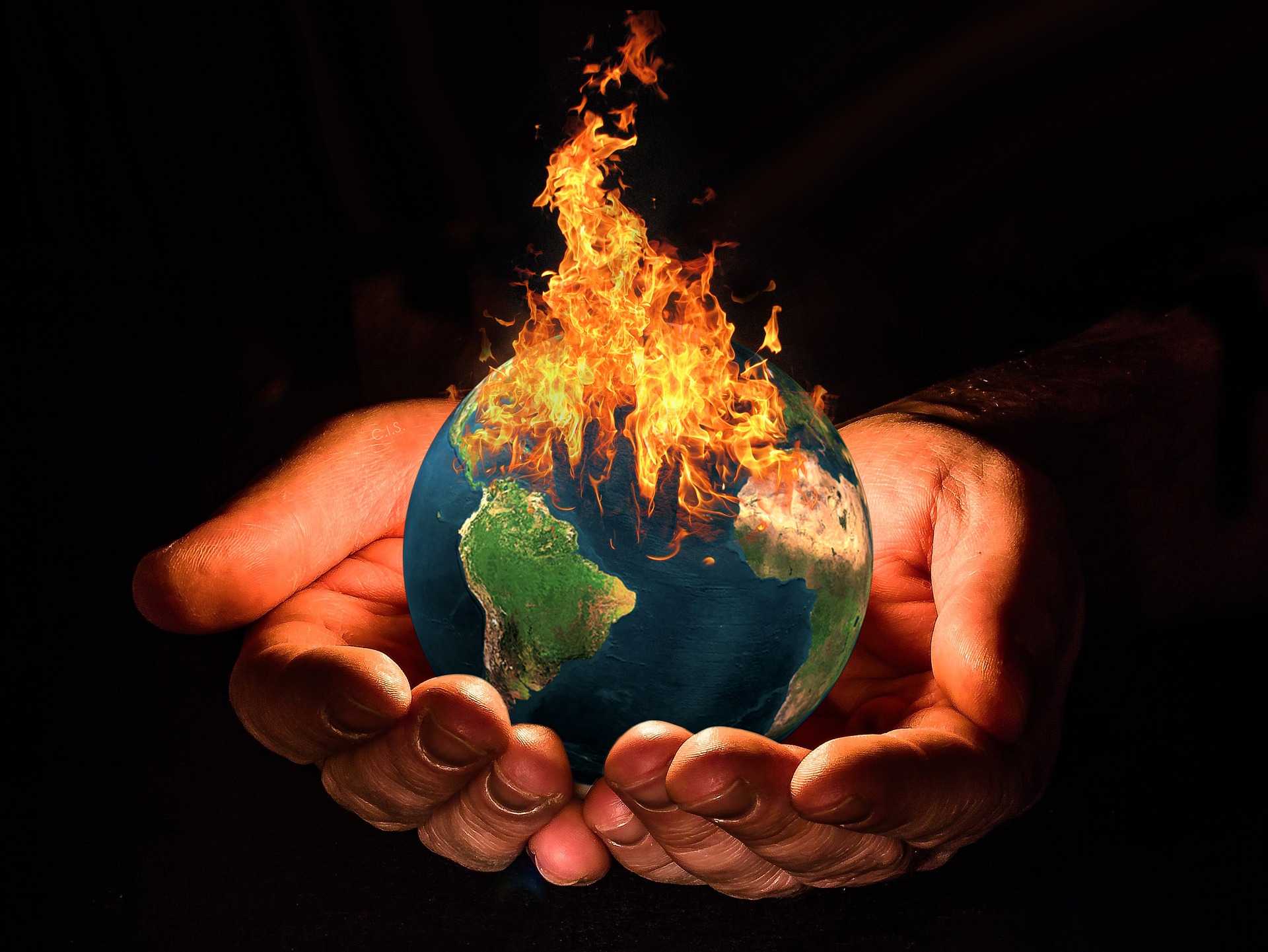 two hands holding out an earth ablaze against dark background