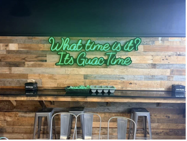 The interior at Guac Time that features a green neon sign and casual space for quick dining