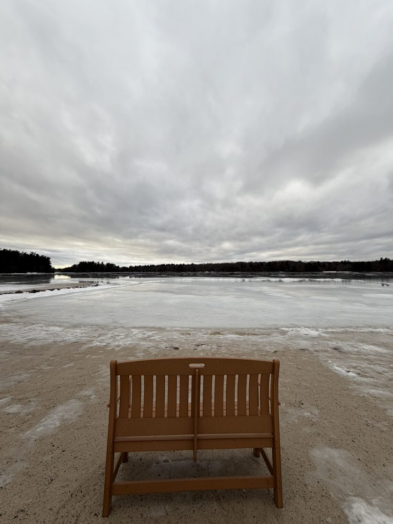 A wooden bench sits facing a snowy lake
