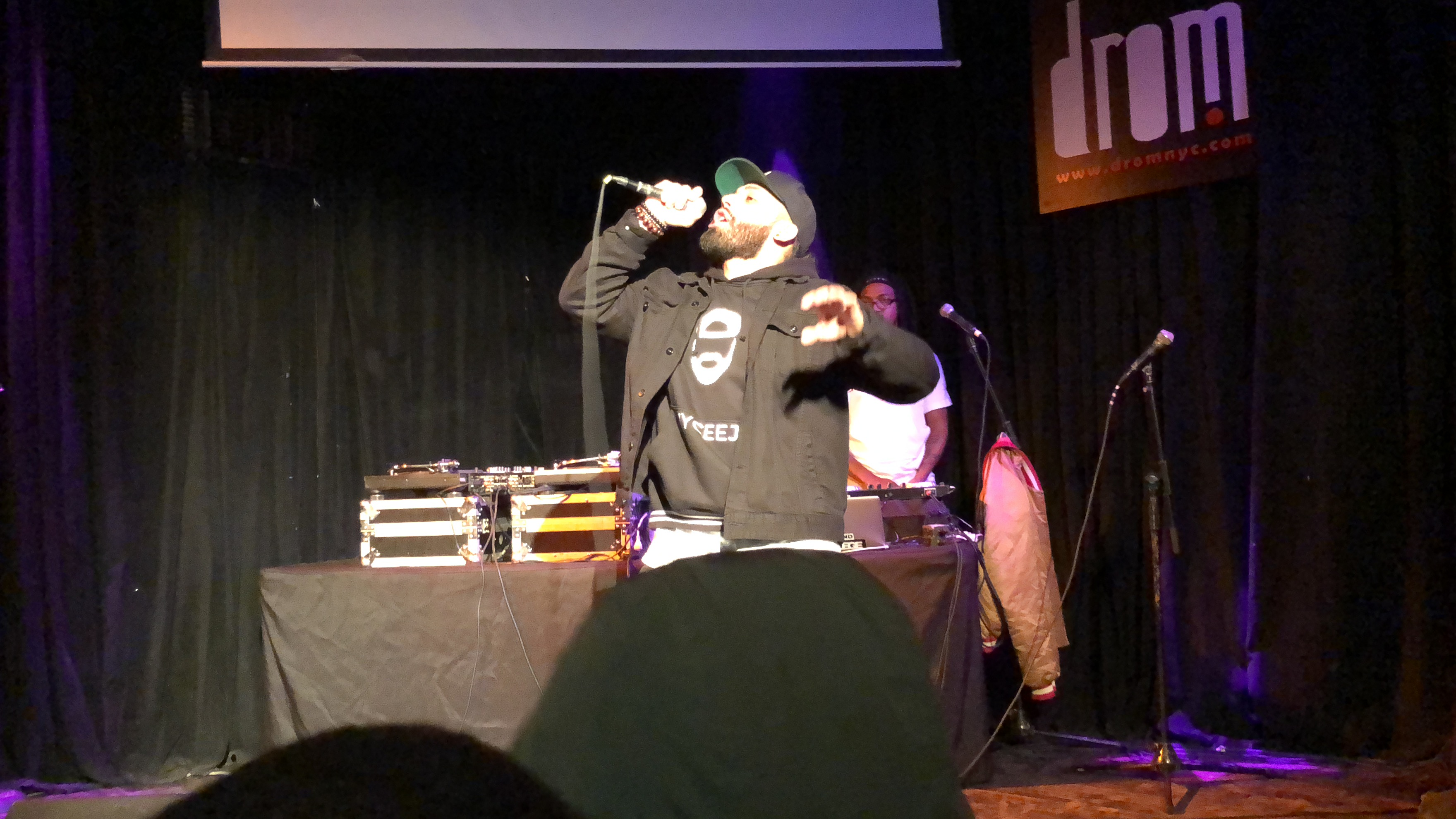 NYCEEJ performing with his head tilted back and arm extended toward the crowd, mic close to his mouth