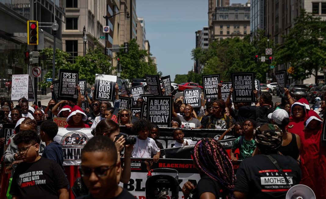 A gathering of Black mothers and children protesting in favor of family reunification. They are holding signs that say phrases such as "A Black child was kidnapped today" and "CPS is genocide."