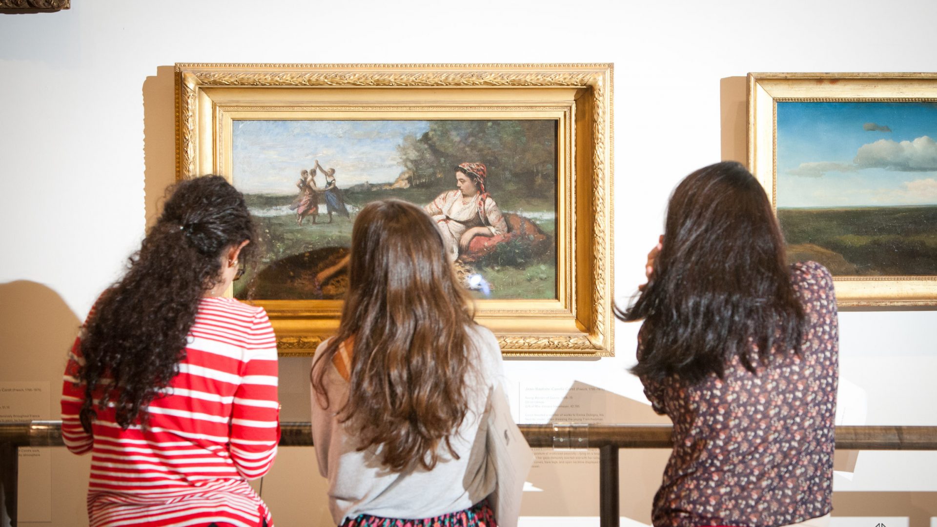 Three students looking closely at a painting in a museum