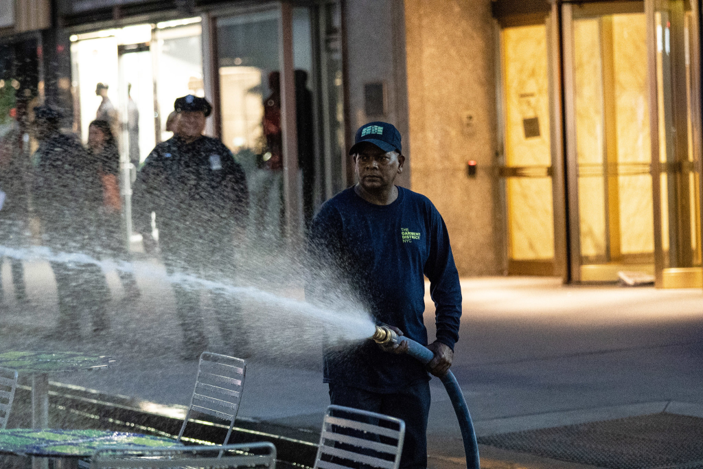 Man spraying water out of a high-power hose at unhoused individuals out of frame