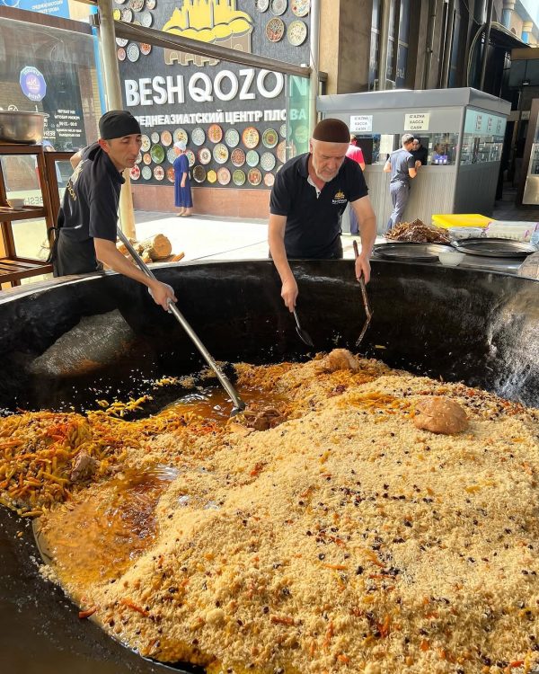 Two men stir a giant cast iron pot filled with food.